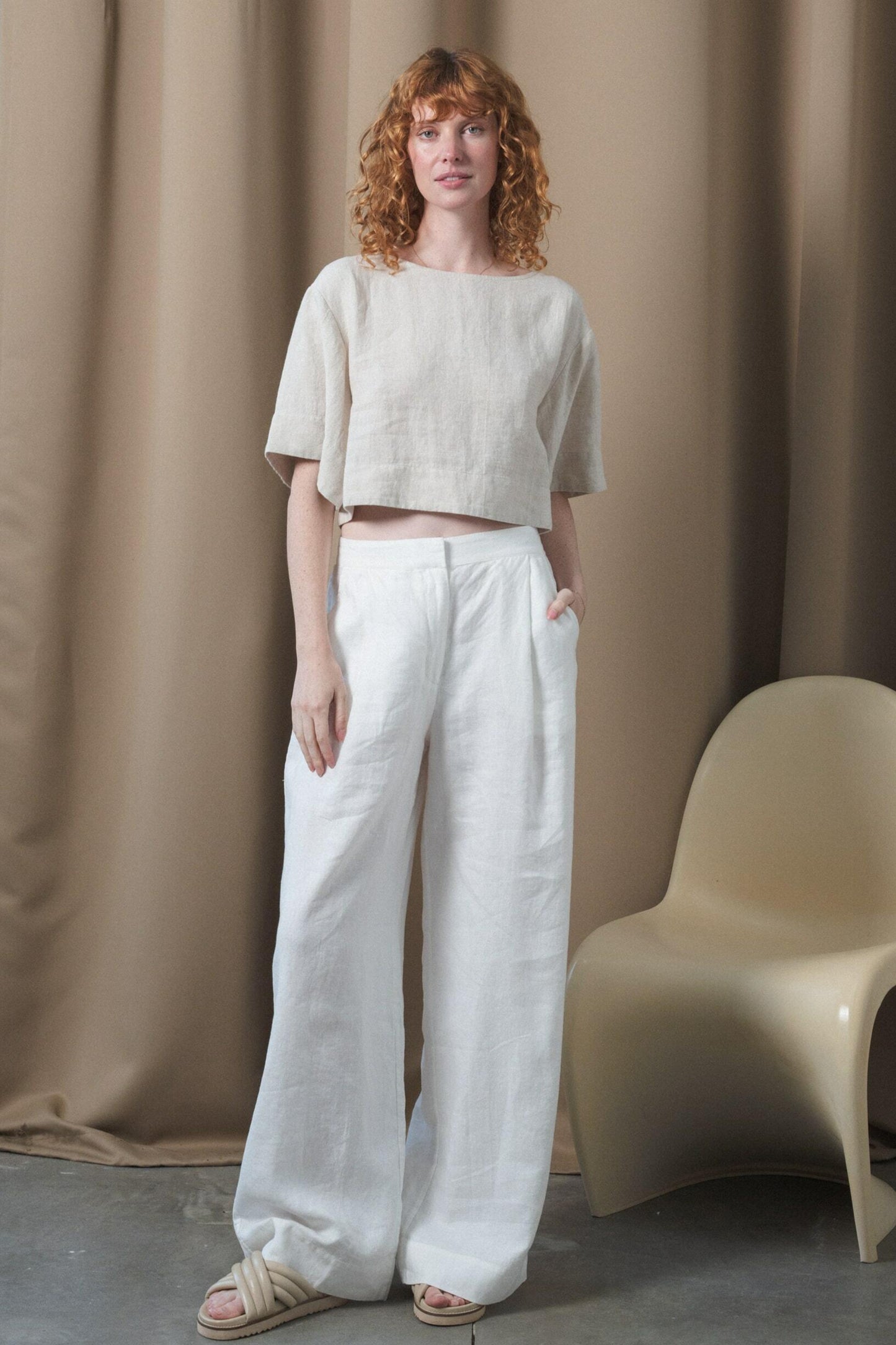 LILLY PILLY Oli linen pants in Ivory standing by a chair