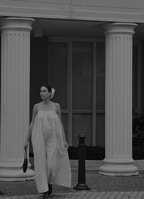 Woman in a LILLY PILLY polka dot linen dress standing between two columns with a building in the background