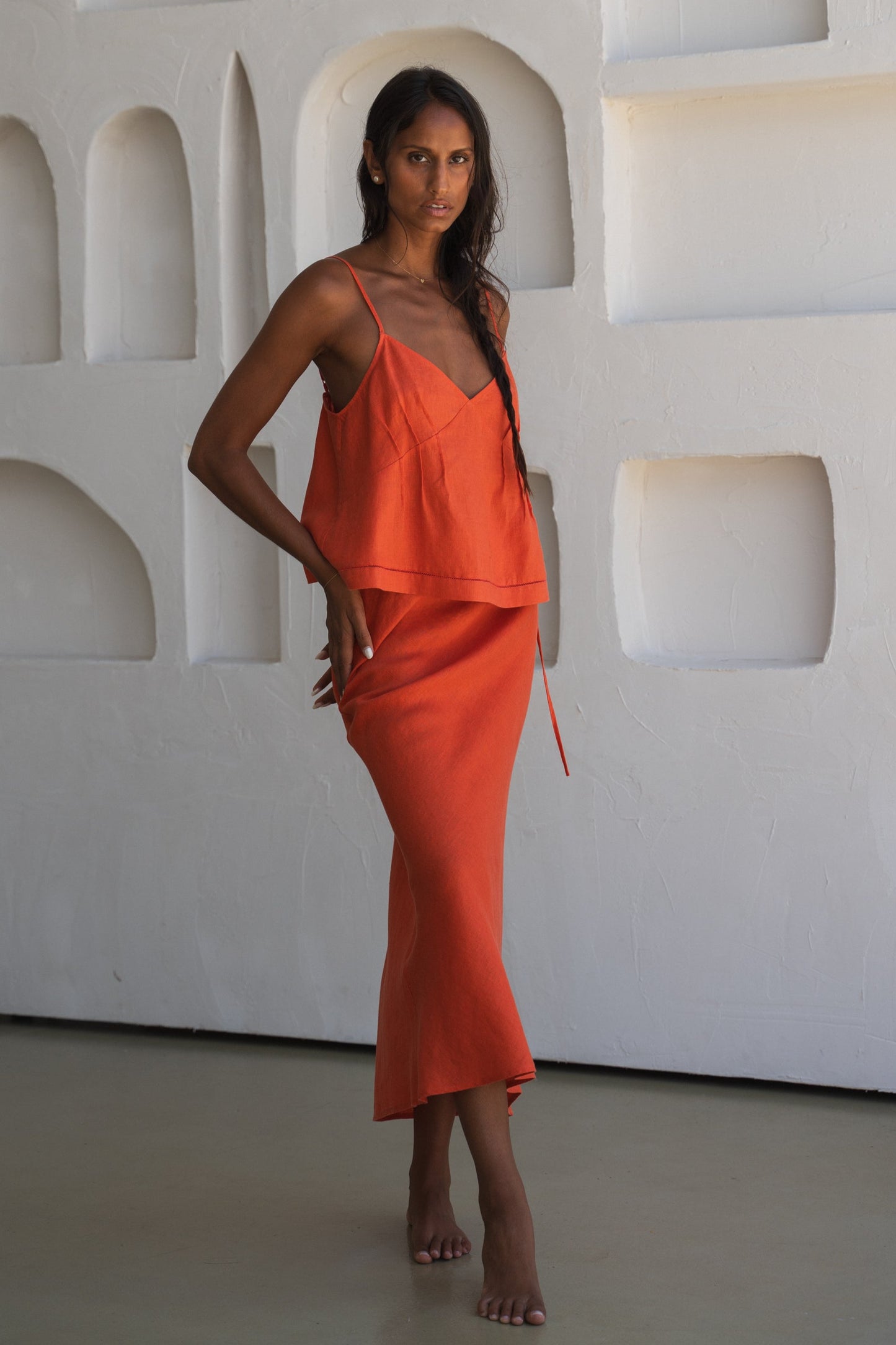 Close up of LILLY PILLY woman wearing a spritz Bea linen cami top with thin straps in a minimal indoor setting against a white wall with geometric shapes.