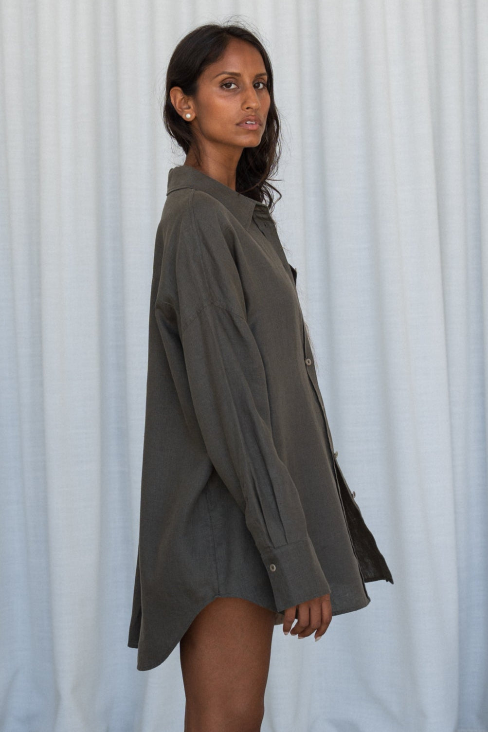 LILY PILLY woman wearing a khaki Kirra linen shirt side view against a white curtain background