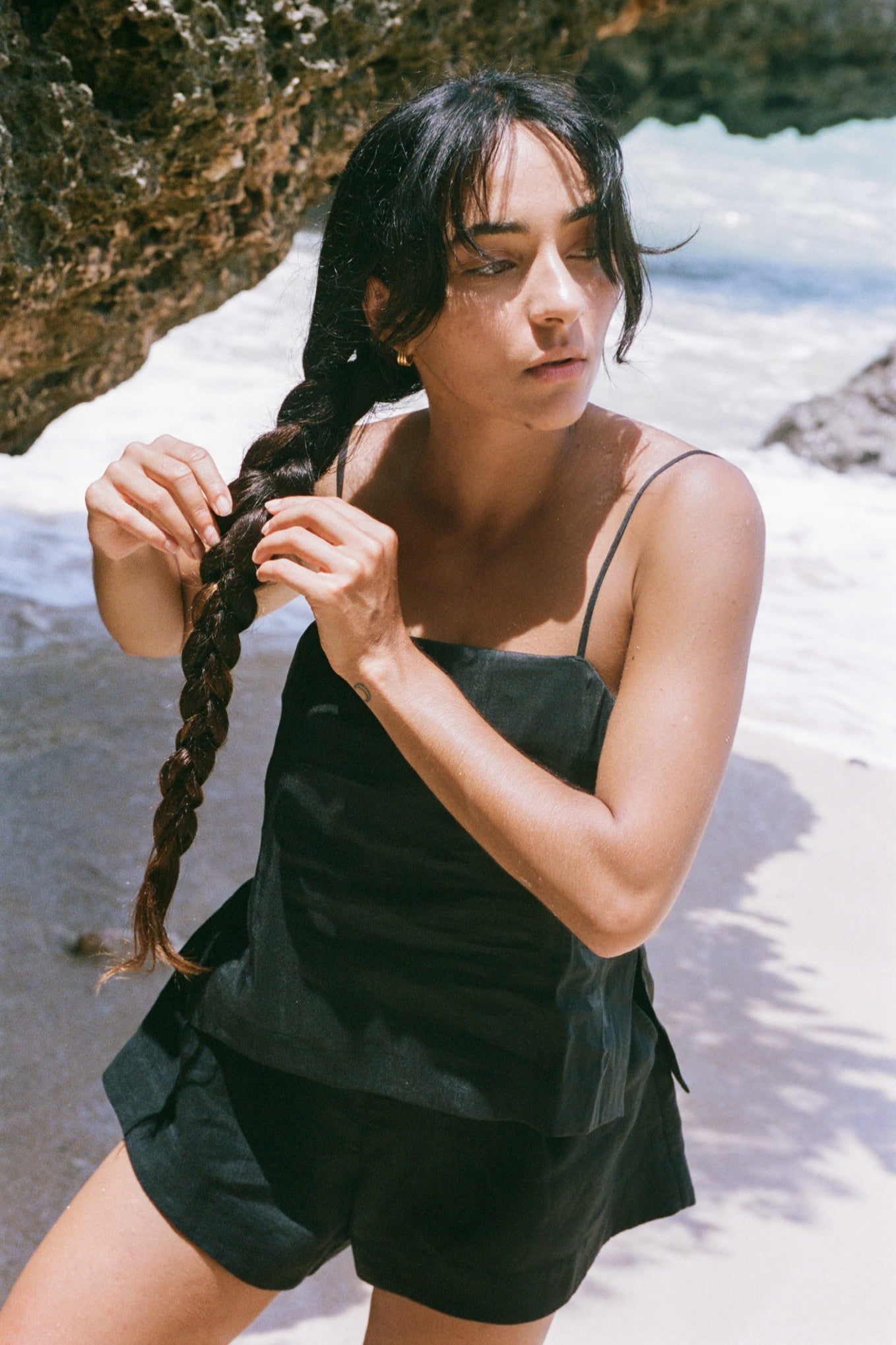 LILLY PILLY woman wearing a black Rosa silk linen cami top and shorts outfit with braided hair standing on a beach