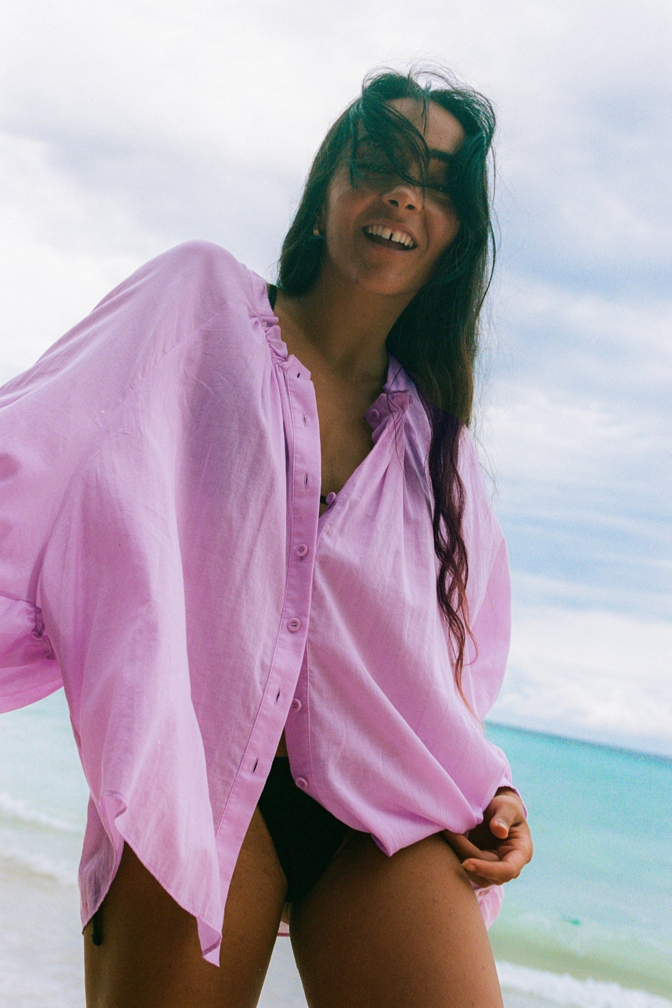 LILLY PILLY woman wearing a orchid Thalia cotton voile shirt blouse over a black bikini on a beach