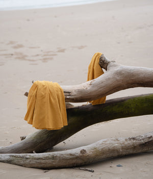 LILLY PILLY organic linen pieces in Sunflower colour laid upon a fallen tree on the beach