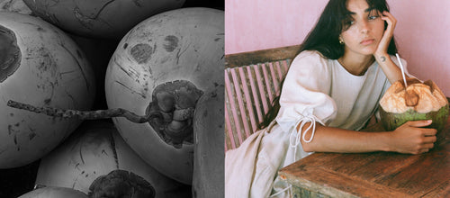 Close-up of textured coconut shells on the left, and a LILLY PILLY girl wearing Charlotte ivory linen  dress while holding a coconut with bread on a wooden table on the right.