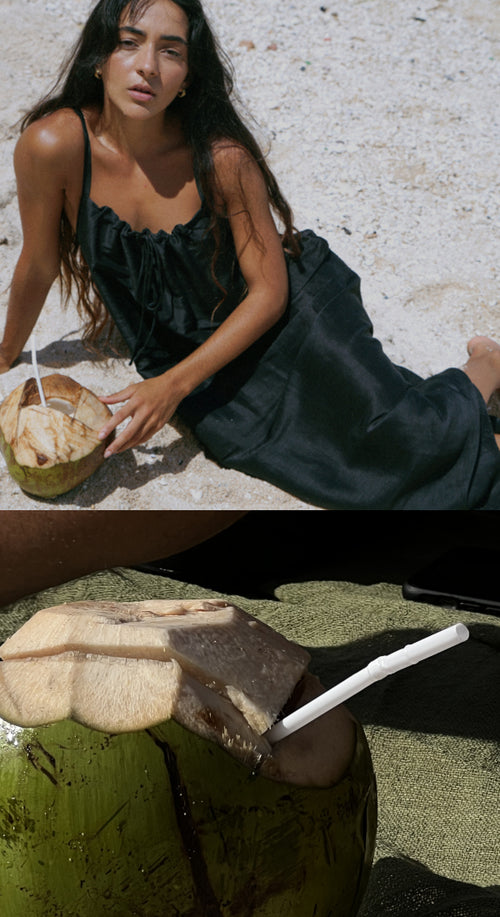 LILLY PILLY woman wearing black Nova silk linen dress sitting on the  beach sipping a fresh coconut